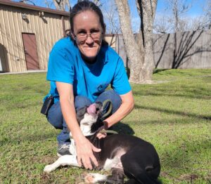 A woman kneeling down next to a dog.